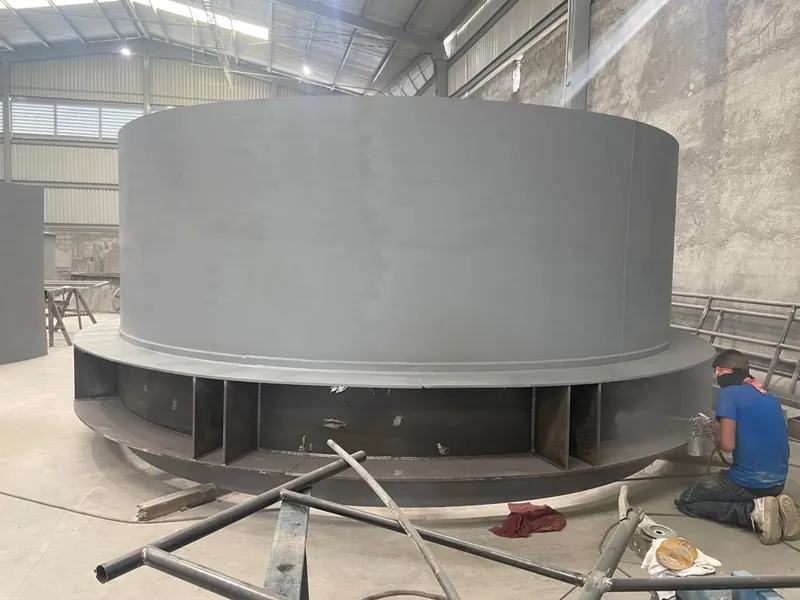 Operario arrodillado junto a un tanque de acero de gran diámetro.